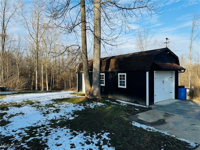 view of snowy exterior with driveway, a garage, an outdoor structure, and a gambrel roof