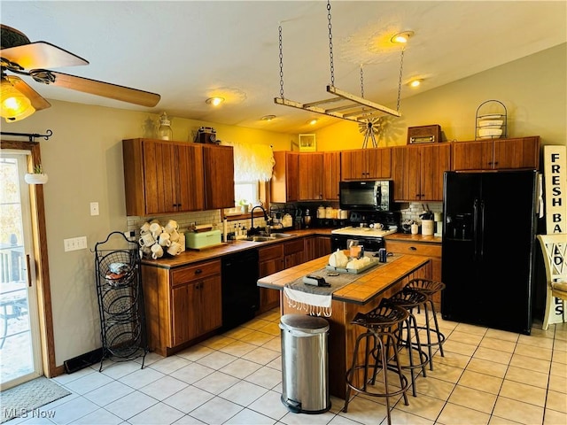 kitchen featuring a center island, light tile patterned floors, lofted ceiling, a sink, and black appliances