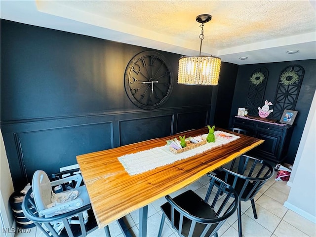 dining space with light tile patterned flooring, a decorative wall, a textured ceiling, and an inviting chandelier