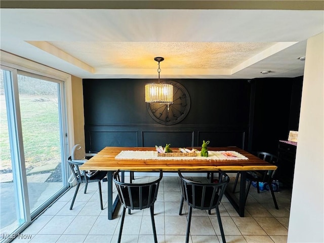 dining area with light tile patterned floors, a tray ceiling, a textured ceiling, and a decorative wall