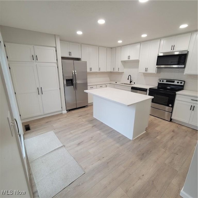 kitchen featuring stainless steel appliances, a sink, white cabinets, light countertops, and a center island