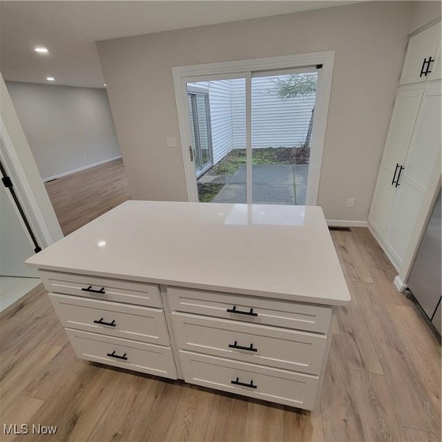 kitchen featuring baseboards, light countertops, light wood-style flooring, and white cabinets