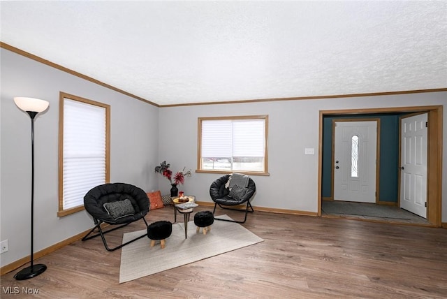 living area featuring ornamental molding, a textured ceiling, baseboards, and wood finished floors