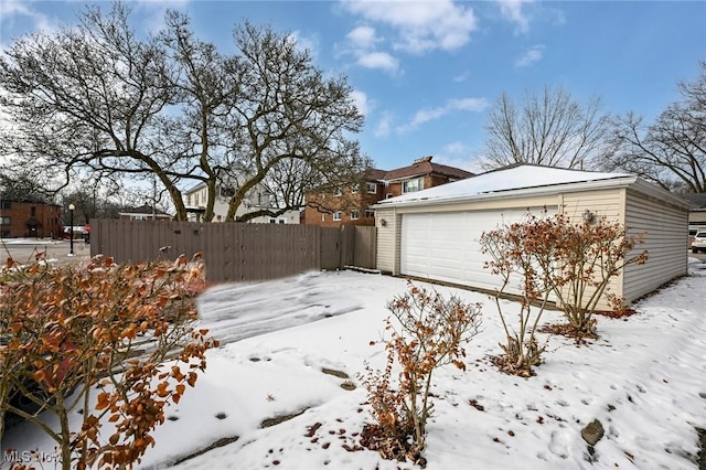 yard layered in snow with an outdoor structure, fence, and a detached garage