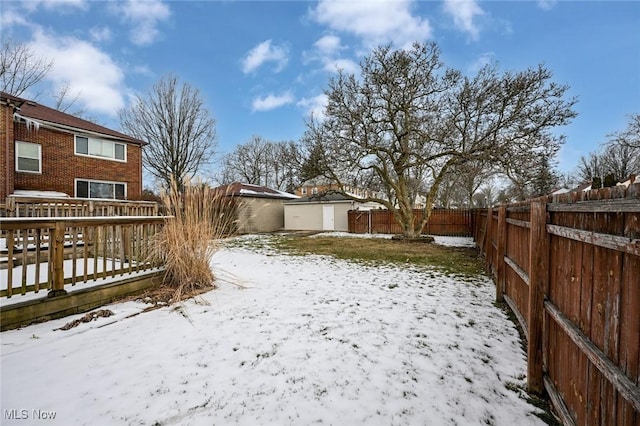 snowy yard with a garage, a fenced backyard, and a wooden deck