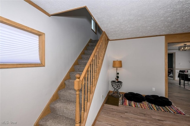 stairs featuring crown molding, a textured ceiling, baseboards, and wood finished floors