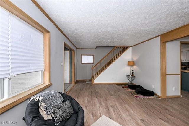 interior space featuring light wood finished floors, baseboards, stairway, crown molding, and a textured ceiling