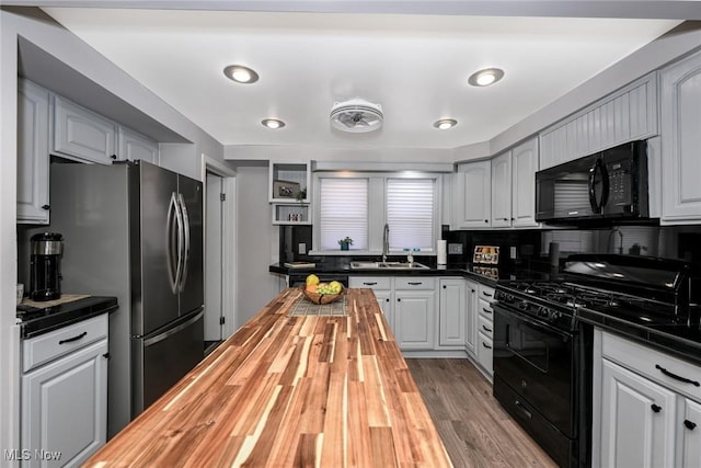 kitchen with wood finished floors, gray cabinets, black appliances, wooden counters, and a sink