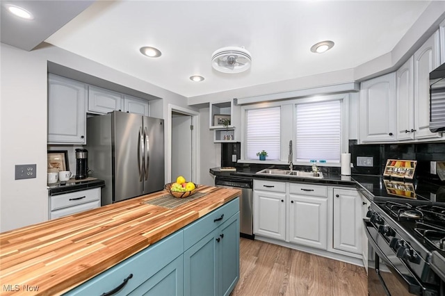 kitchen with blue cabinets, a sink, wooden counters, appliances with stainless steel finishes, and light wood-type flooring