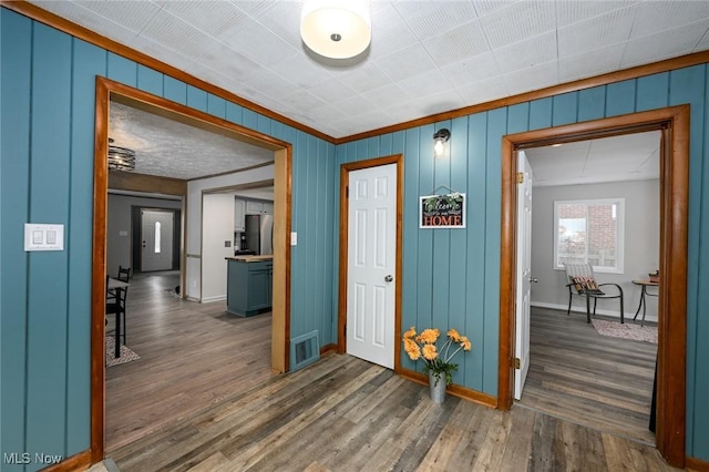 hall with dark wood-style flooring, visible vents, crown molding, and baseboards