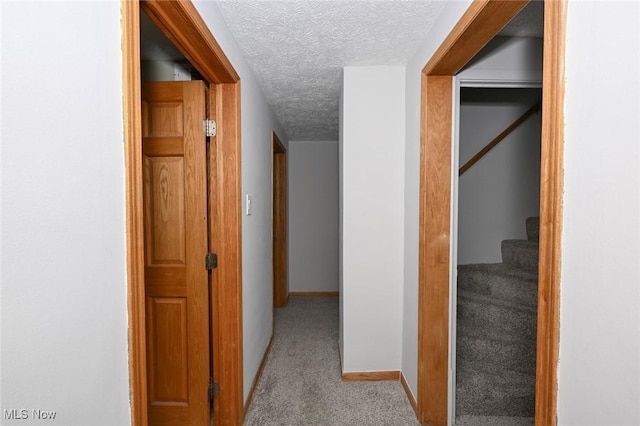 corridor featuring stairway, light colored carpet, a textured ceiling, and baseboards