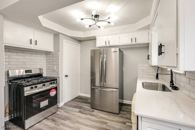 kitchen featuring stainless steel appliances, a raised ceiling, white cabinetry, a sink, and light stone countertops