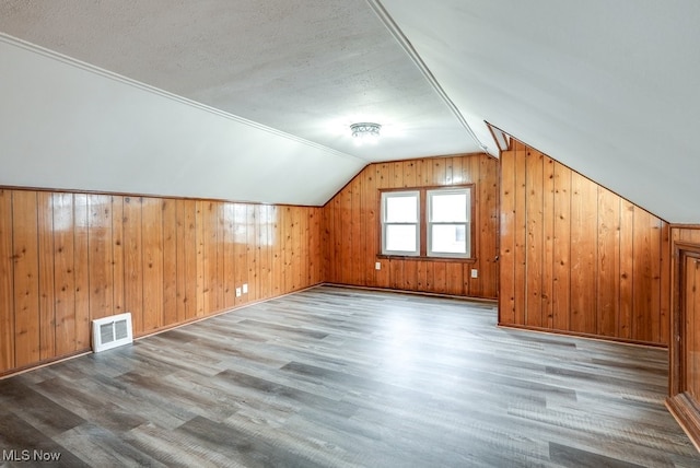 bonus room featuring visible vents, light wood-style flooring, wood walls, vaulted ceiling, and a textured ceiling