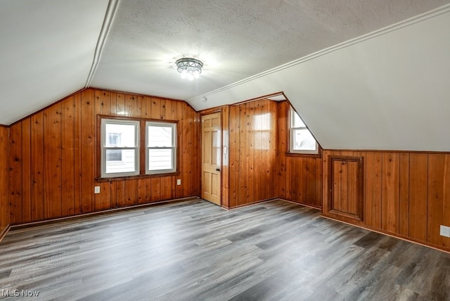 additional living space featuring vaulted ceiling, wood walls, light wood finished floors, and a textured ceiling