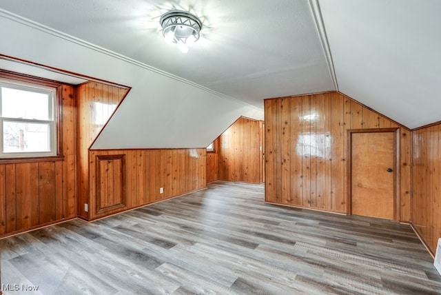 bonus room with lofted ceiling, light wood finished floors, and wooden walls