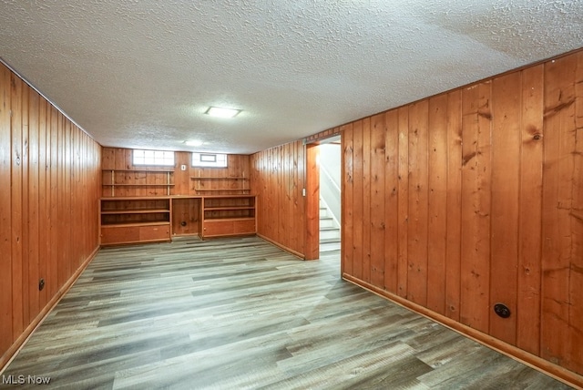 spare room with light wood-style flooring, wooden walls, a textured ceiling, and stairs