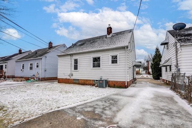 rear view of house featuring central AC, a chimney, and roof with shingles