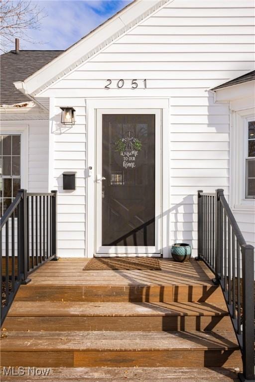 view of exterior entry with roof with shingles and a wooden deck