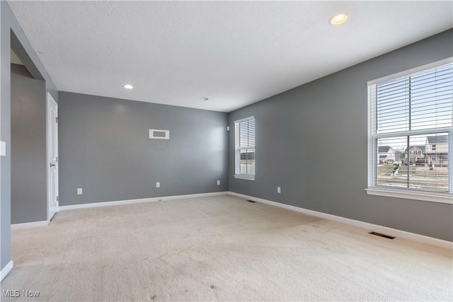 unfurnished room featuring visible vents, light carpet, baseboards, and a textured ceiling