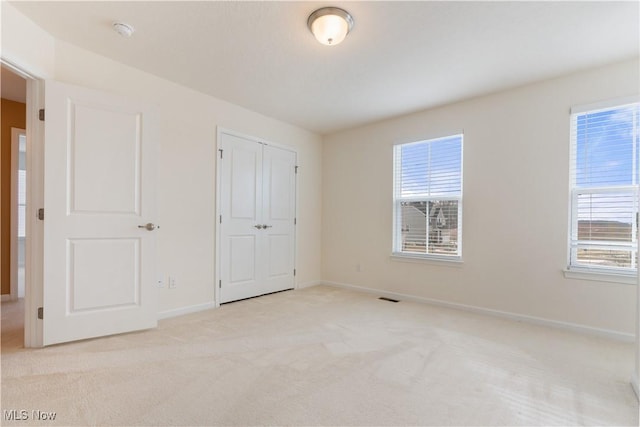 unfurnished bedroom featuring baseboards, multiple windows, visible vents, and light colored carpet