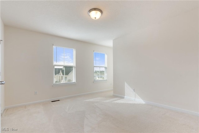 spare room featuring light colored carpet, visible vents, and baseboards