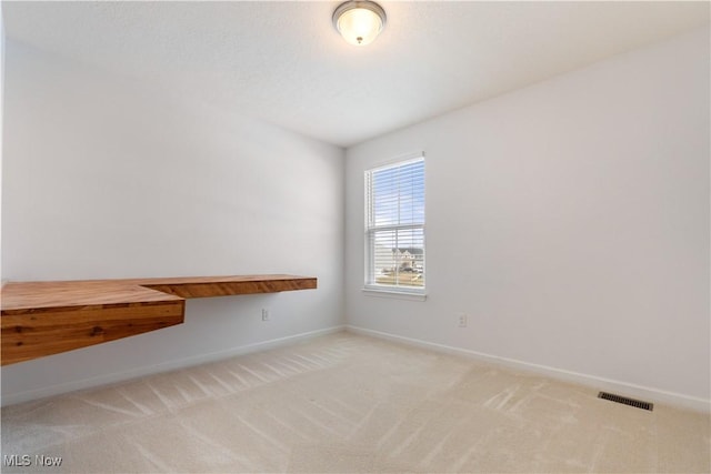 empty room with baseboards, visible vents, and light colored carpet