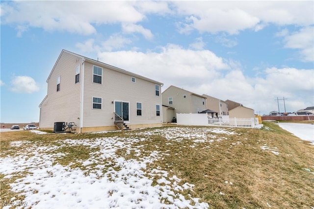 snow covered property with entry steps, fence, and central AC