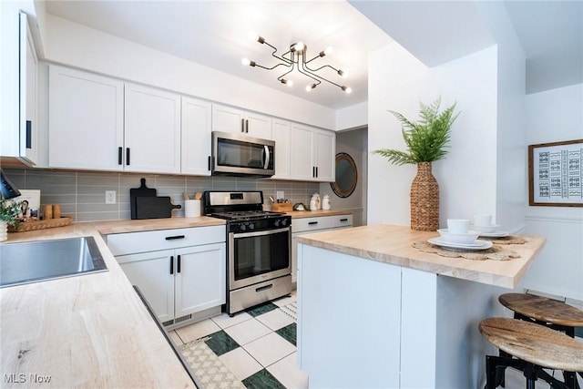 kitchen with appliances with stainless steel finishes, a breakfast bar area, light countertops, white cabinetry, and backsplash