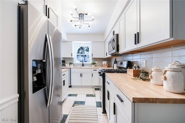 kitchen featuring a sink, white cabinets, wooden counters, appliances with stainless steel finishes, and tasteful backsplash