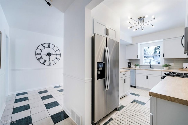 kitchen with tasteful backsplash, appliances with stainless steel finishes, light countertops, white cabinetry, and a sink