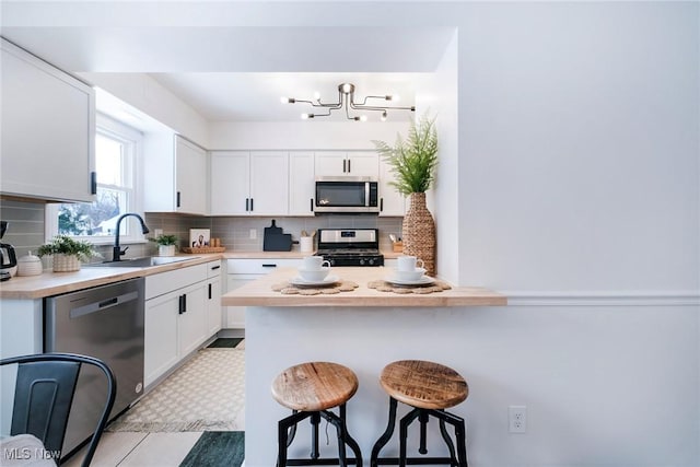 kitchen featuring a breakfast bar area, a sink, white cabinets, light countertops, and appliances with stainless steel finishes