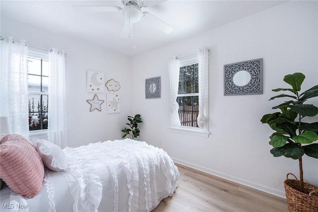 bedroom featuring baseboards, multiple windows, ceiling fan, and light wood finished floors