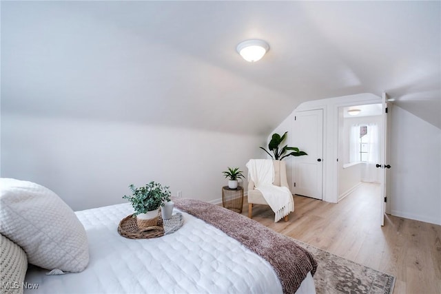 bedroom with light wood-type flooring, baseboards, and lofted ceiling