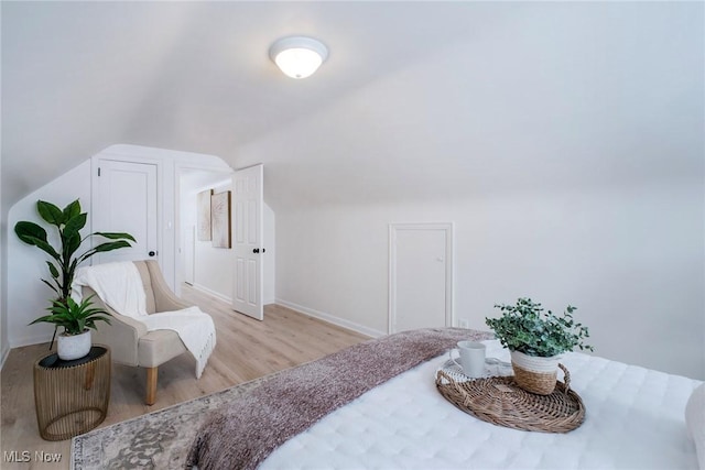 bedroom with lofted ceiling, light wood-style flooring, and baseboards