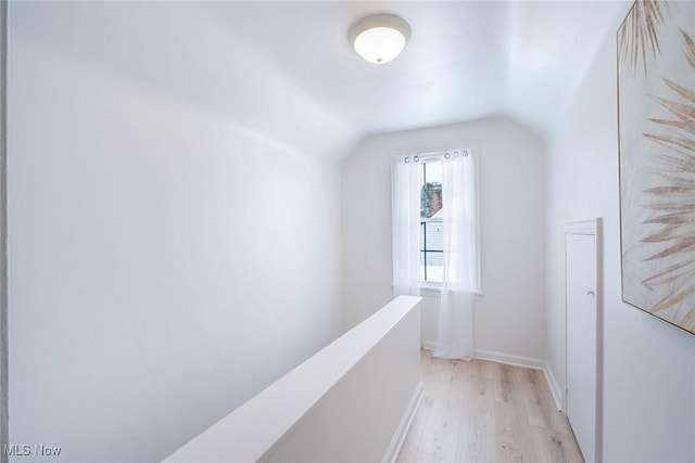 hall featuring an upstairs landing, vaulted ceiling, light wood-style flooring, and baseboards