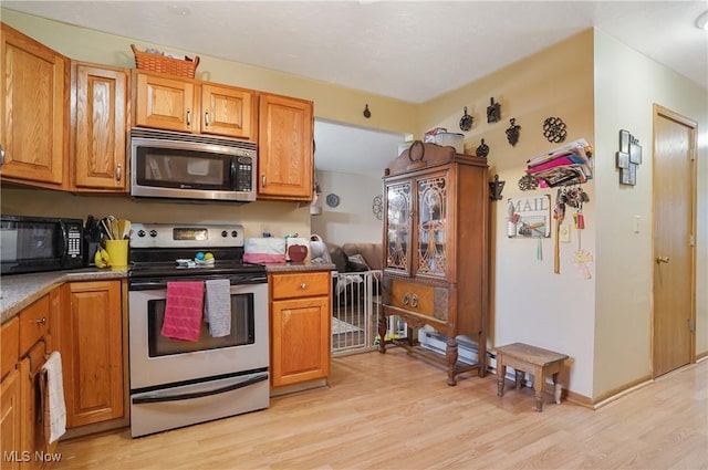 kitchen with light wood finished floors, appliances with stainless steel finishes, brown cabinetry, and baseboards