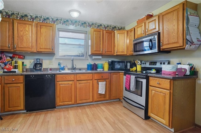 kitchen featuring brown cabinets, dark countertops, a sink, light wood-type flooring, and black appliances