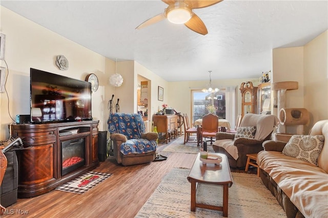 living room featuring a glass covered fireplace, light wood-style flooring, and ceiling fan with notable chandelier