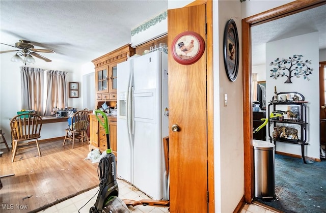 kitchen featuring a textured ceiling, a ceiling fan, built in study area, white fridge with ice dispenser, and glass insert cabinets