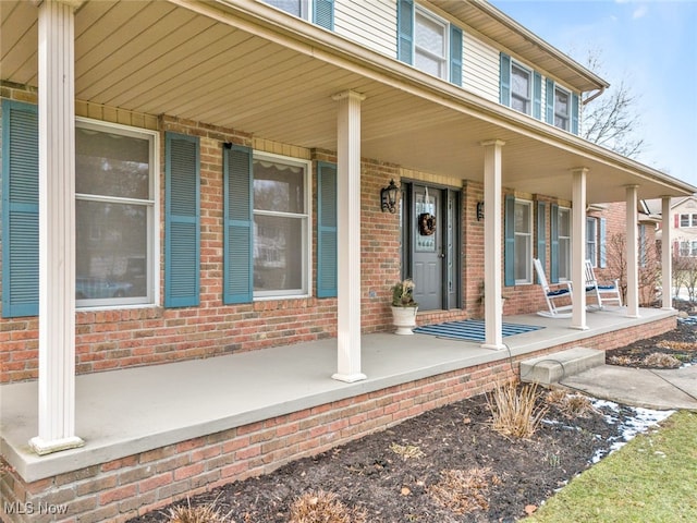 doorway to property featuring covered porch and brick siding