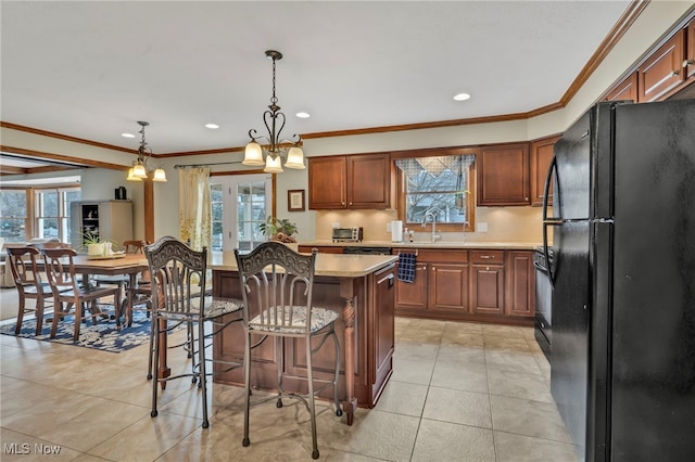 kitchen featuring a sink, a kitchen island, light countertops, freestanding refrigerator, and decorative light fixtures