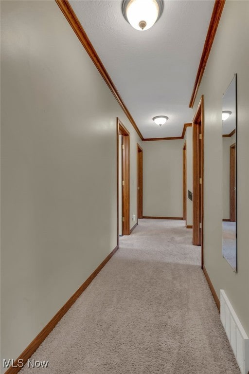 hall with ornamental molding, light colored carpet, visible vents, and baseboards