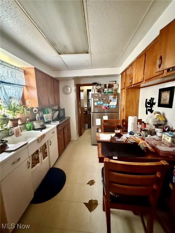 kitchen with brown cabinets, light tile patterned floors, freestanding refrigerator, and a sink