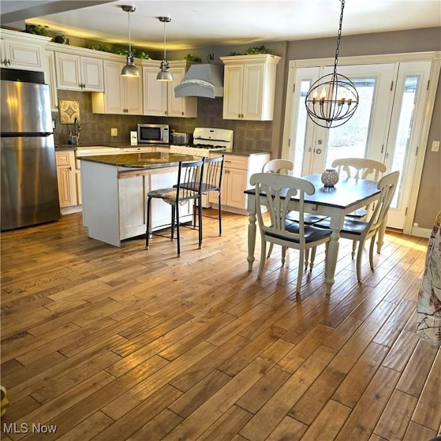 kitchen featuring a center island, decorative light fixtures, light wood finished floors, appliances with stainless steel finishes, and premium range hood