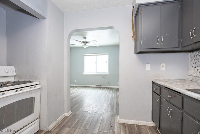 kitchen featuring arched walkways, dark wood-style floors, white range with electric stovetop, and gray cabinetry