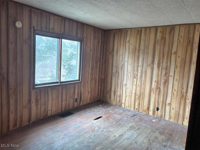 unfurnished room featuring visible vents, wood walls, and a textured ceiling