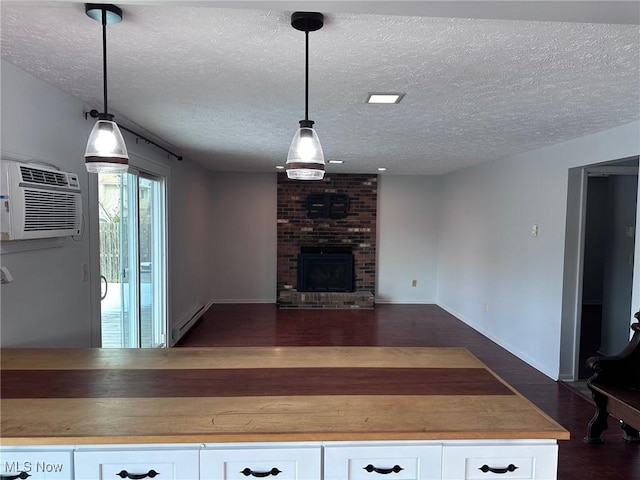 unfurnished living room featuring dark wood-style flooring, a fireplace, a baseboard radiator, an AC wall unit, and a textured ceiling