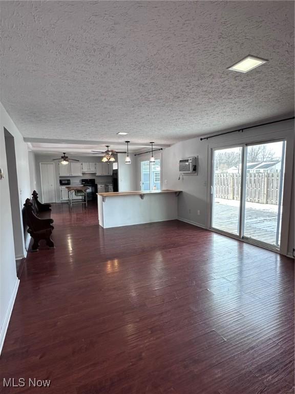 unfurnished living room featuring a textured ceiling, ceiling fan, baseboards, a wall mounted AC, and dark wood finished floors