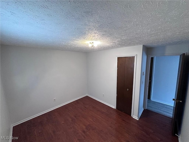 unfurnished room with a textured ceiling, dark wood-style flooring, and baseboards