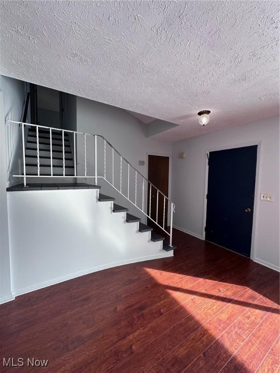 foyer entrance featuring dark wood-style floors, stairs, baseboards, and a textured ceiling